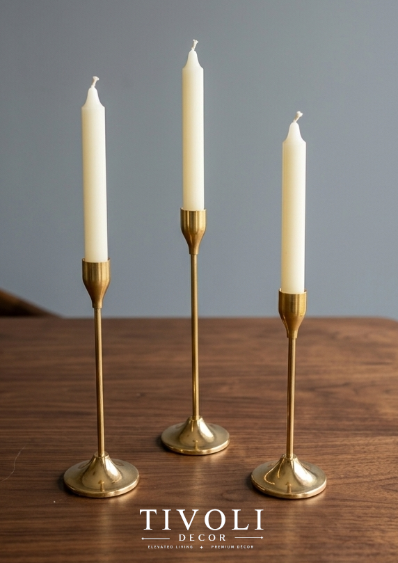 Branded Tivoli Decor 3-piece luxury gold taper candlestick holder set styled with white candles on a dark walnut wood table surface.