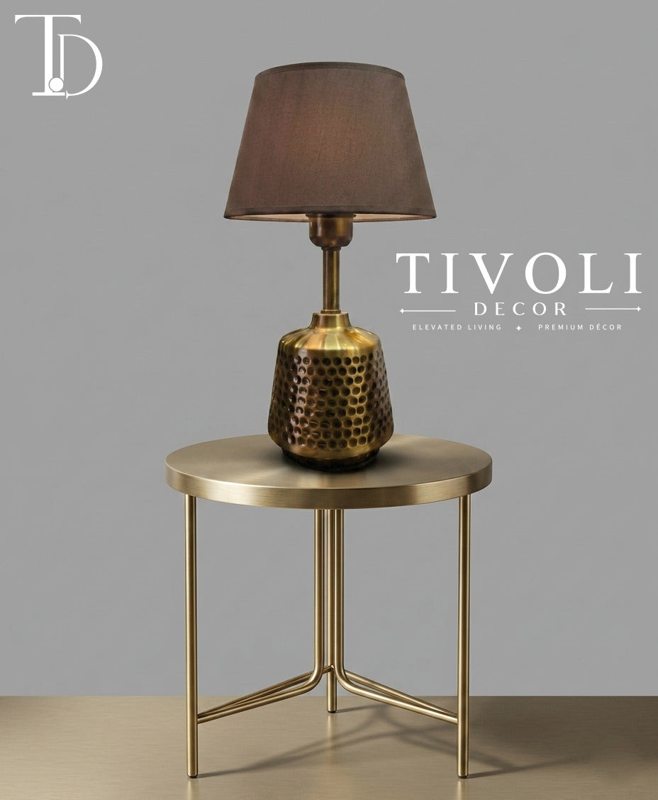 Branded Tivoli Decor luxury table lamp with a honeycomb textured brass base and dark fabric shade styled on a round gold metal side table.