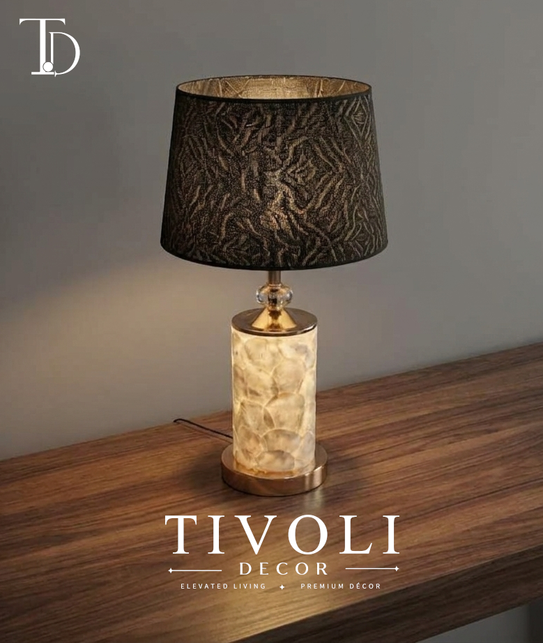Branded Tivoli Decor luxury table lamp with an illuminated mother of pearl column base, faceted crystal sphere accent, and textured black and gold fabric shade on a wood table.