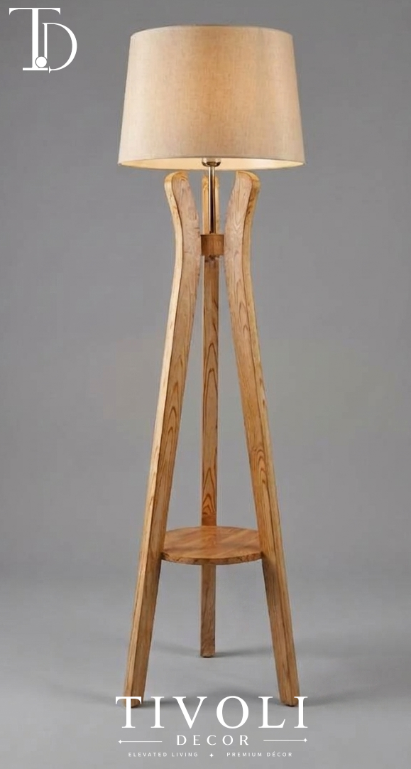 Branded Tivoli Decor sculptural wooden tripod floor lamp with curved ash wood legs, integrated display shelf, and a warm beige linen shade against a grey background.