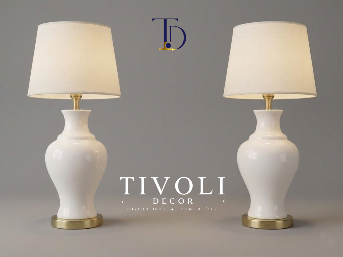 Pair of branded Tivoli Decor luxury table lamps with smooth high gloss white ceramic bases and ivory fabric shades standing symmetrically on a grey studio background.
