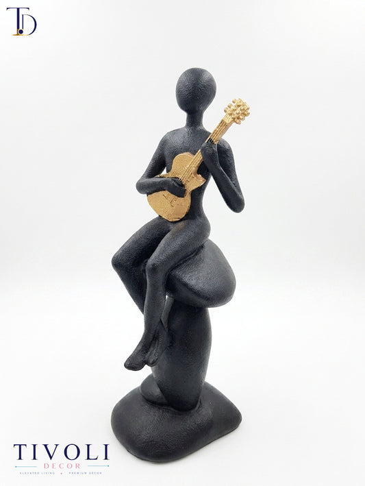 Modern volcanic black musician statue with a golden guitar by Tivoli Decor, a premium abstract decoration piece for living room console tables in Pakistan.