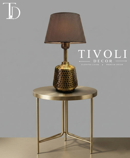 Branded Tivoli Decor luxury table lamp with a honeycomb textured brass base and dark fabric shade styled on a round gold metal side table.