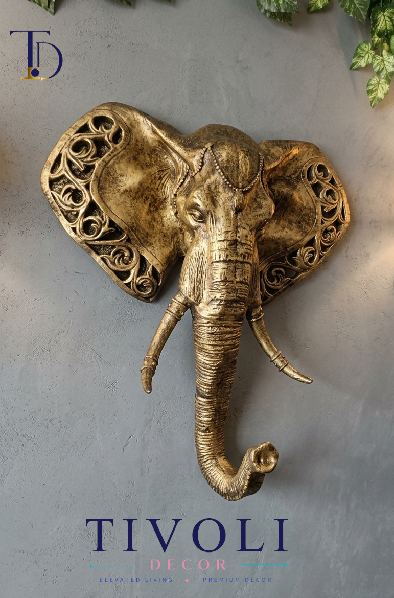 Royal antique gold elephant head 3D wall sculpture with carved filigree ear details by Tivoli Decor, mounted on a gray concrete wall in Pakistan.