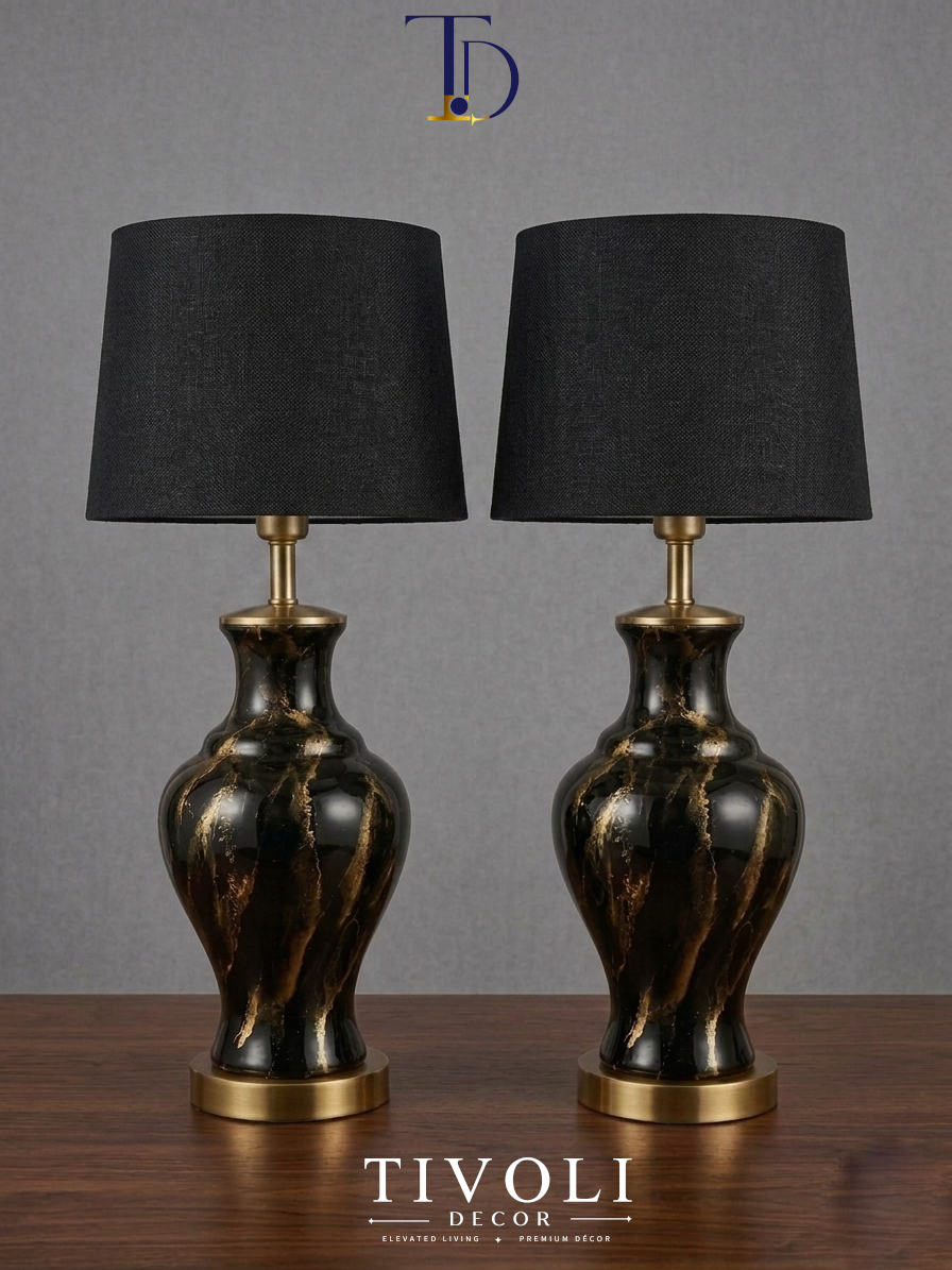 Pair of branded Tivoli Decor luxury black ceramic table lamps with gold marble veins and dark black fabric shades standing symmetrically on a dark wooden table.