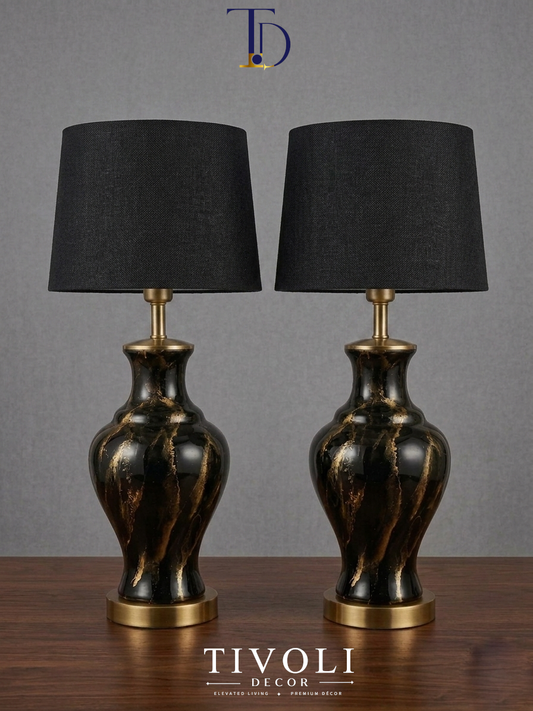 Pair of branded Tivoli Decor luxury black ceramic table lamps with gold marble veins and dark black fabric shades standing symmetrically on a dark wooden table.