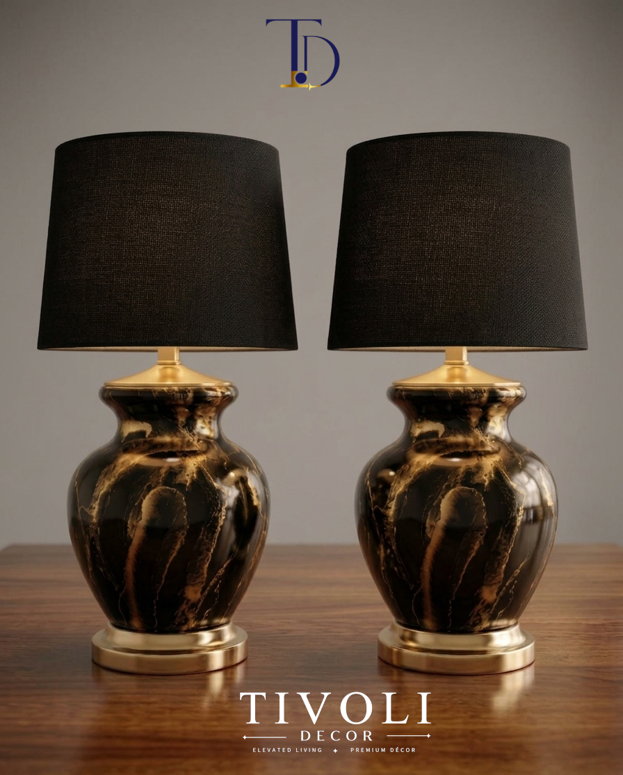Pair of branded Tivoli Decor luxury table lamps with wide gilded brushed gold bases, black and gold marble ceramic bodies, and black fabric shades on a wood surface.