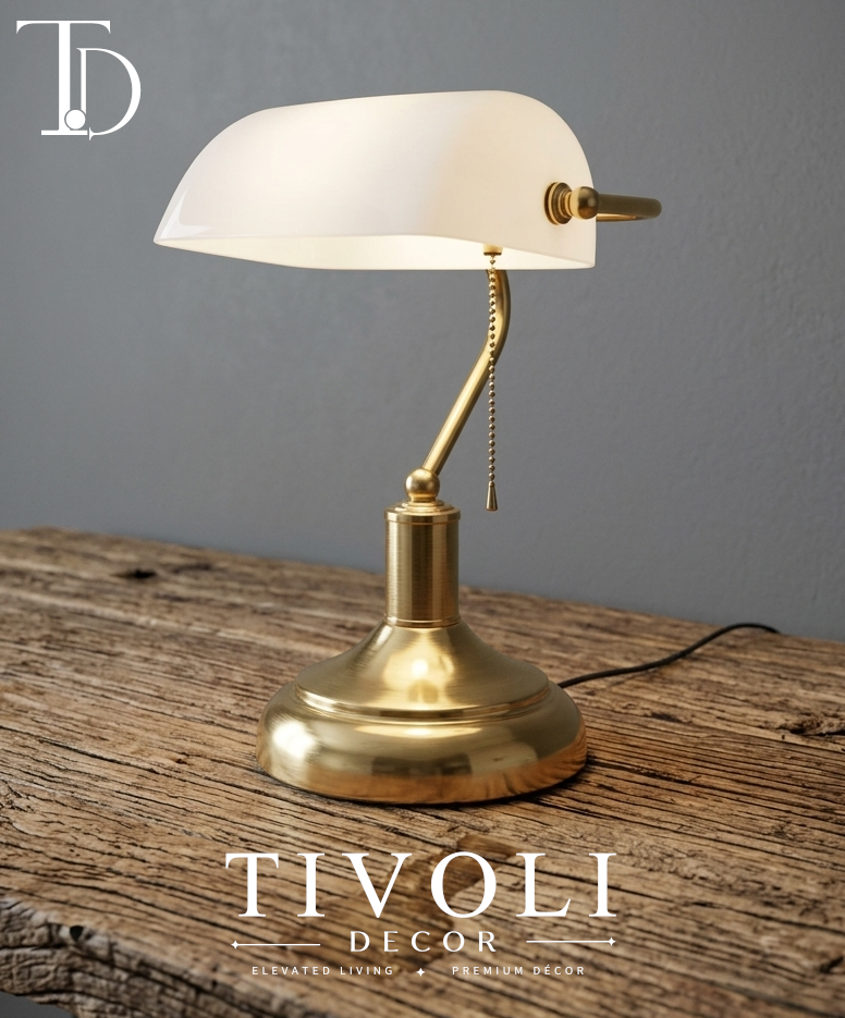 Branded Tivoli Decor luxury bankers lamp with a high gloss white glass shade and gold brushed brass base sitting illuminated on a rustic wood desk surface.