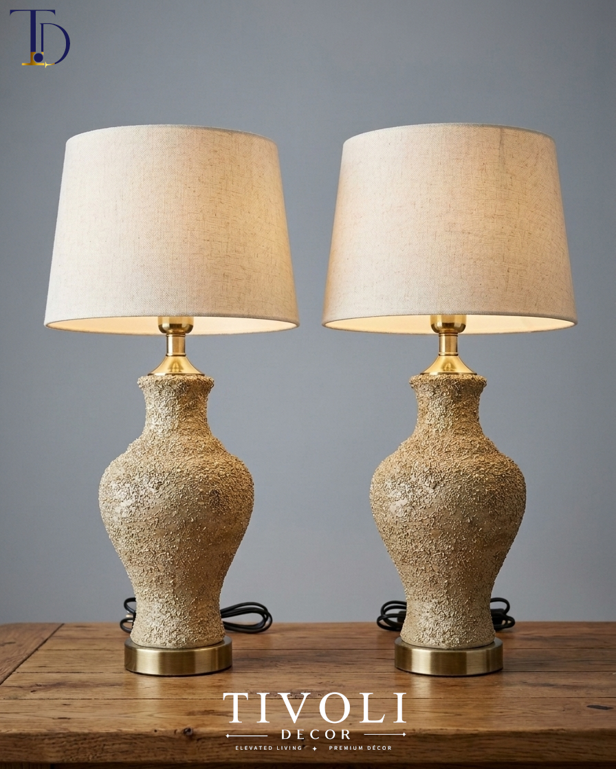Pair of branded Tivoli Decor luxury table lamps with heavily textured sand beige volcanic stone ceramic bases and cream fabric shades styled on a wood table.