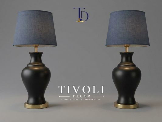Pair of branded Tivoli Decor luxury table lamps with smooth satin matte black ceramic bases, gold pedestals, and slate blue linen fabric shades against a grey background.