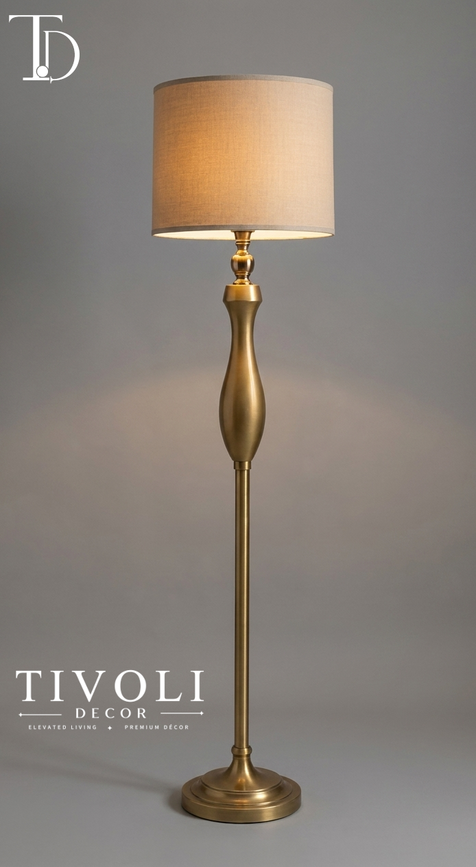 Branded Tivoli Decor luxury antique brass floor lamp with a sculpted trophy style gold stem and beige linen drum shade against a grey studio background.