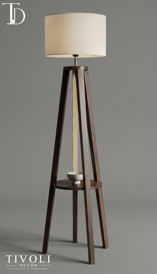 Branded Tivoli Decor minimalist wooden tripod floor lamp with a built-in display shelf holding a ceramic bowl, topped with a cream linen shade against a grey background.