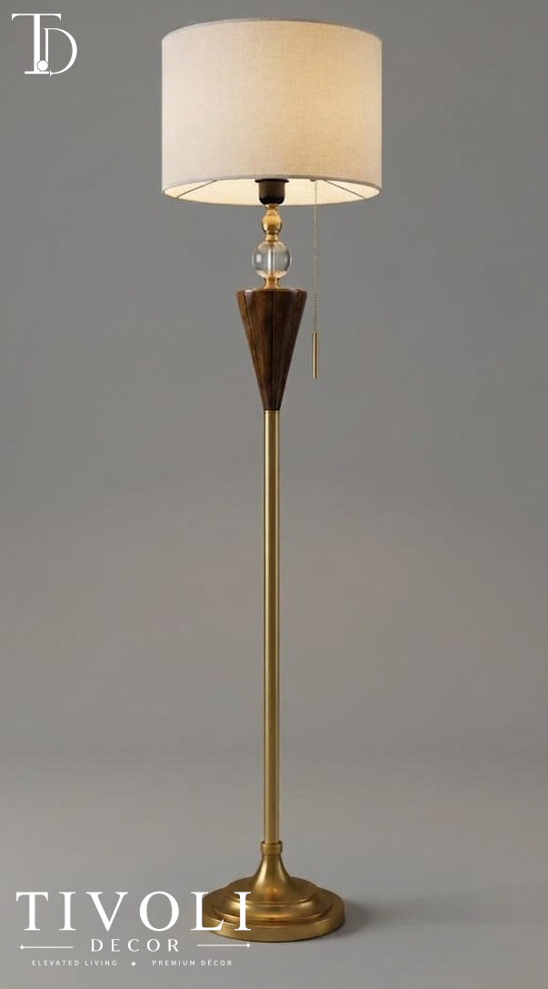 Branded Tivoli Decor luxury brushed brass floor lamp with a walnut wood cone element, crystal ball detailing, and a cream linen shade against a grey background.