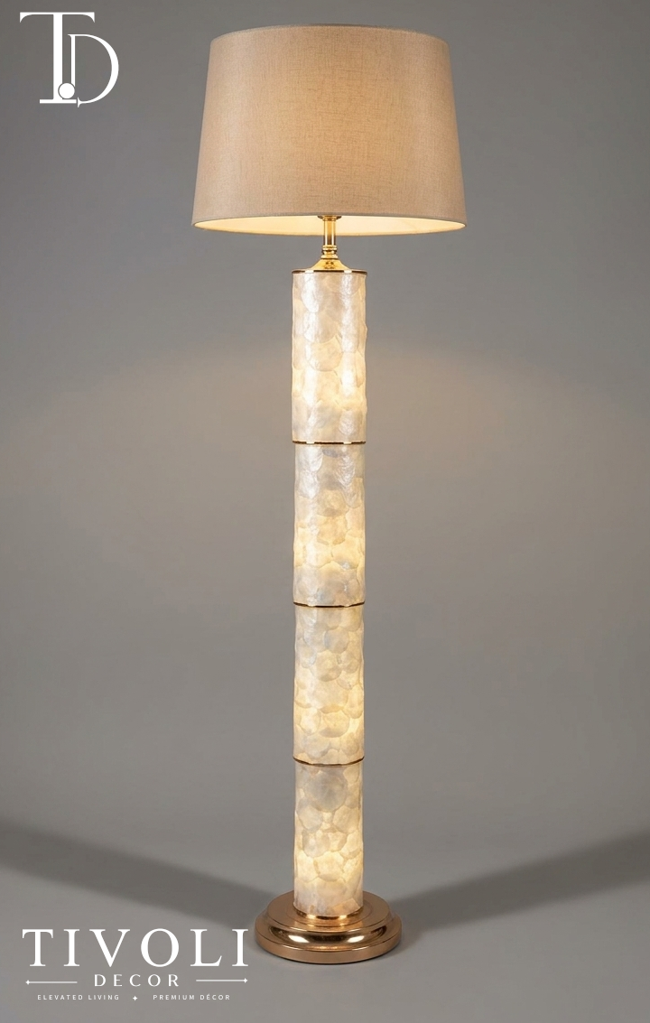 Branded Tivoli Decor luxury gold floor lamp with an illuminated multi tiered mother of pearl column accent and warm beige linen shade against a grey background.