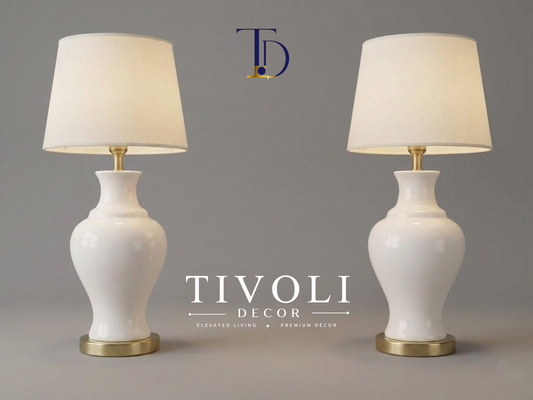 Pair of branded Tivoli Decor luxury table lamps with smooth high gloss white ceramic bases and ivory fabric shades standing symmetrically on a grey studio background.