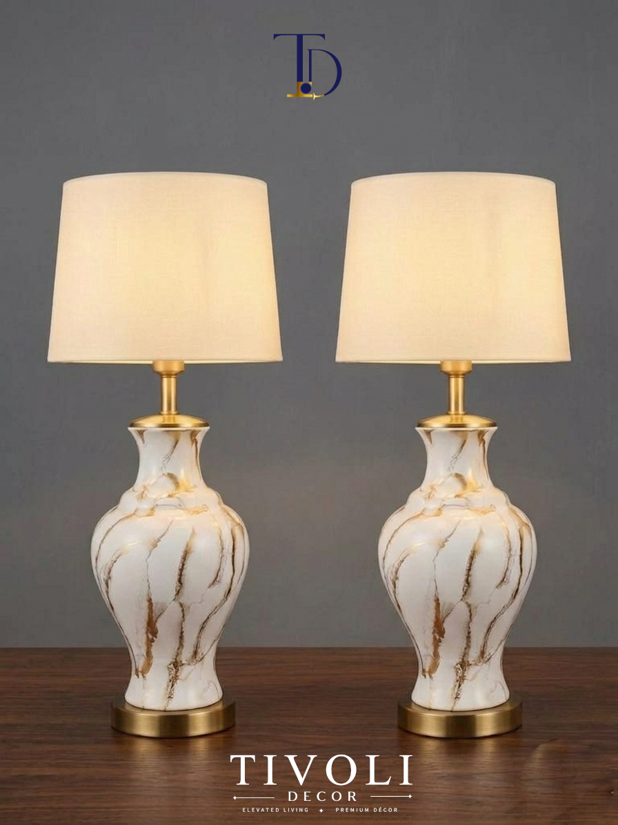 Pair of Tivoli Decor luxury white ceramic table lamps with hand painted gold marble veins and cream linen shades standing symmetrically on a dark wooden table.