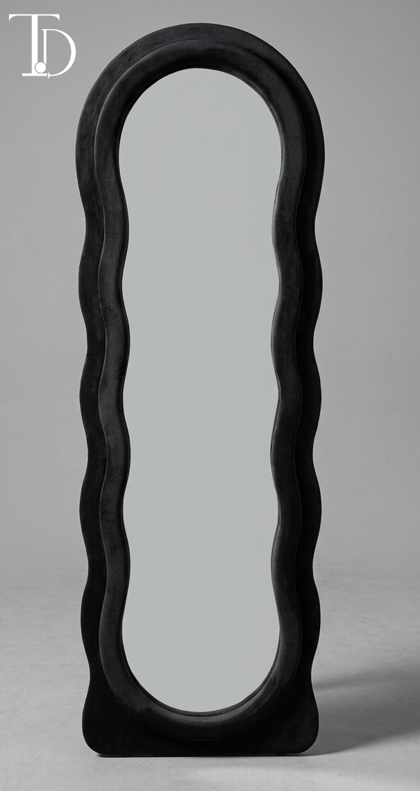 Branded Tivoli Decor Nero irregular wavy full-length floor mirror upholstered in a thick plush midnight black velvet fabric lining against a grey studio background.