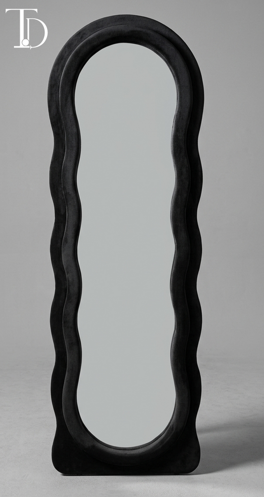 Branded Tivoli Decor Nero irregular wavy full-length floor mirror upholstered in a thick plush midnight black velvet fabric lining against a grey studio background.