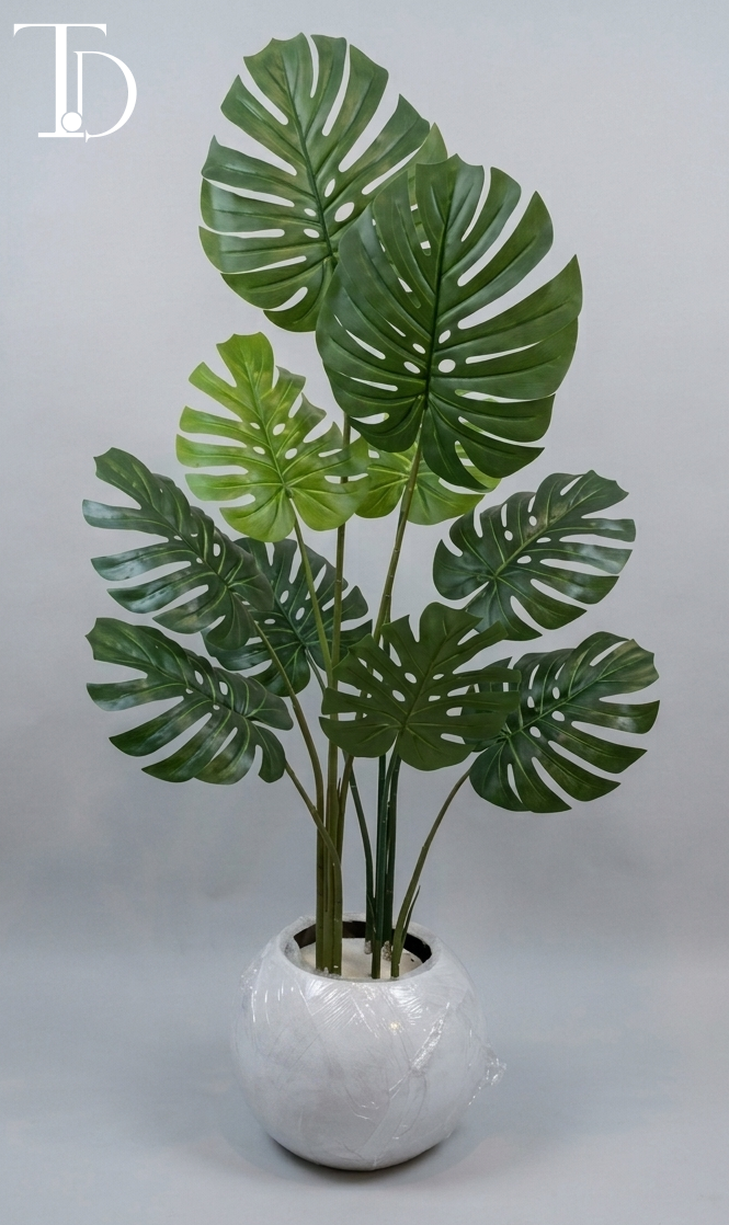 Branded Tivoli Decor luxury artificial monstera deliciosa tree with iconic green split leaves standing in a glossy white spherical orb planter against a grey studio background.