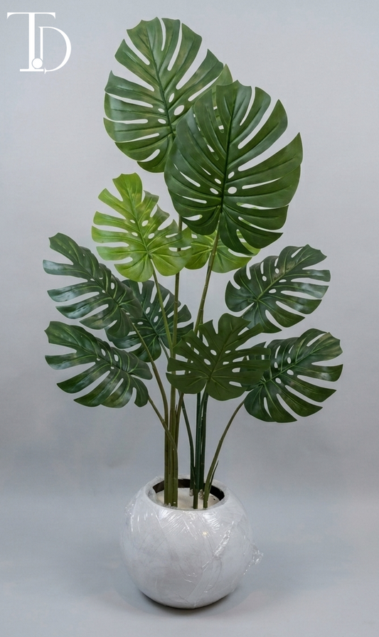 Branded Tivoli Decor luxury artificial monstera deliciosa tree with iconic green split leaves standing in a glossy white spherical orb planter against a grey studio background.