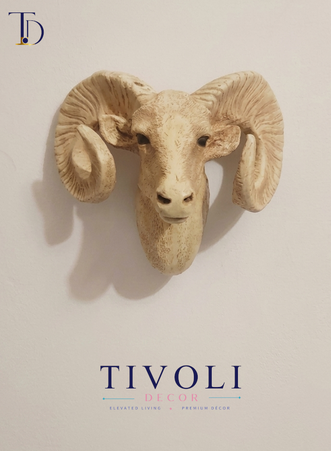 Weathered ivory-finish ram head wall sculpture with curled horns mounted on cream wall